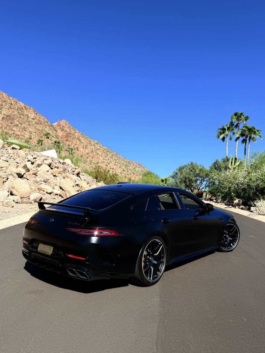 Matte black Mercedes-AMG GT 63 S with a rear wing, parked below the mountains